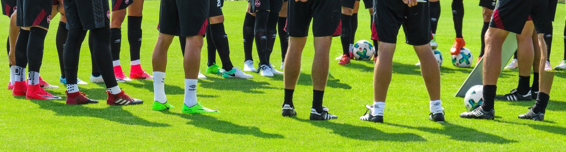 Männerbeine auf einer Wiese mit Fußball