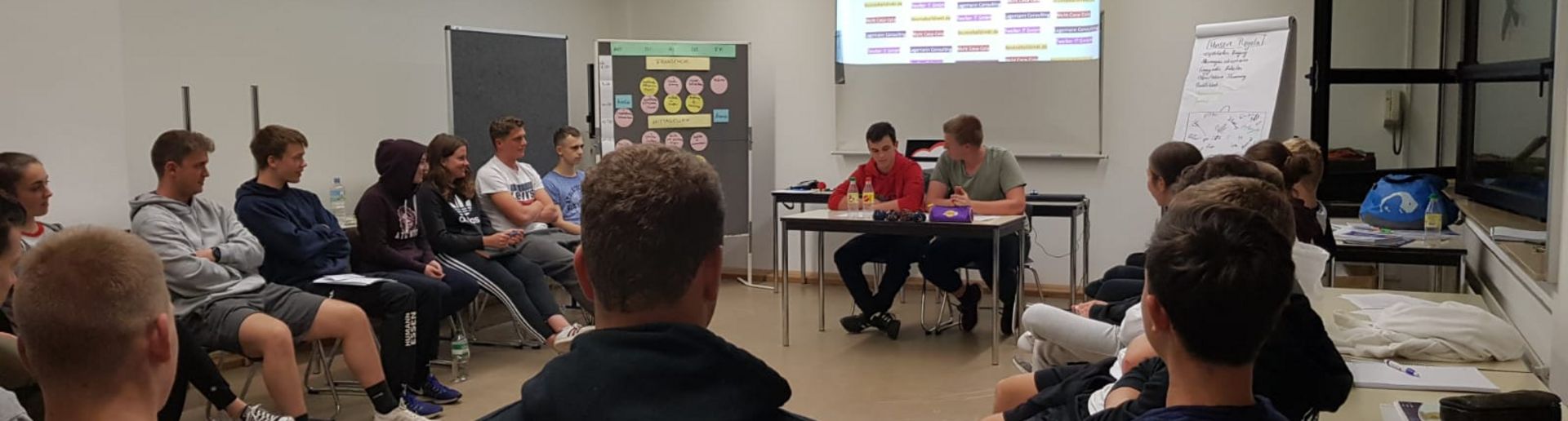 Junge Menschen sitzen in einem Stuhlkreis und hören einen Vortrag